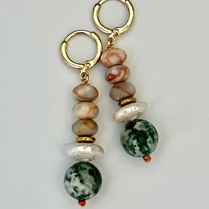 The SELENA EARRINGS by SANDRINE FRANCE STUDIO are gold hoops with stacked beige and brown marbled beads, a white pearl-like accent, gold spacer, and a large green-and-white Tree Agate bead, displayed on a plain background.