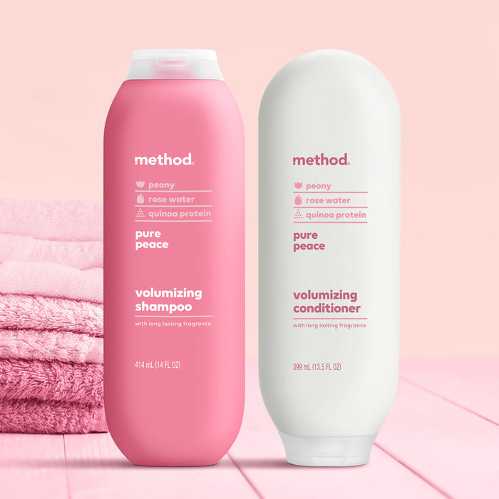 Two Method hair products sit on a wooden surface: a pink volumizing shampoo and a white volumizing conditioner made with peony, rose water, and quinoa protein. Pink towels in the background highlight their cruelty-free ingredients.