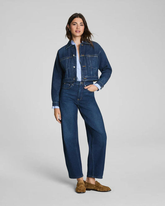 A person wearing SPANX BARREL LEG JEANS by SPANX in dark blue, paired with a light blue rolled-up sleeve shirt and brown moccasin loafers, shown from the back.