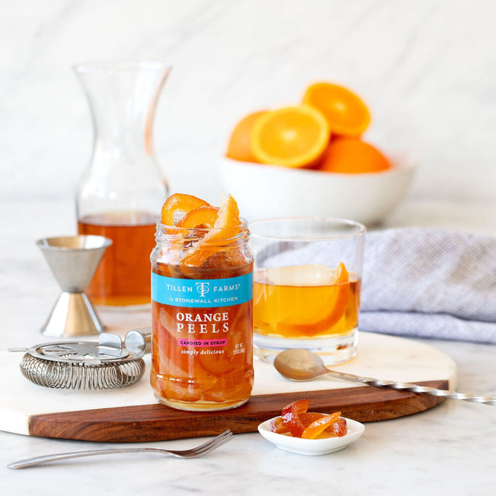 A jar of Stonewall Kitchen - Tillen Farms Candied Orange Peels with a turquoise lid invites you to indulge in a citrusy treat. The label, adorned with umbrellas and waves design details, proudly displays "Candied Orange Peels in Syrup, Simply Delicious," and it has a net weight of 12 oz. Enjoy this vegan delight from Stonewall Kitchen!