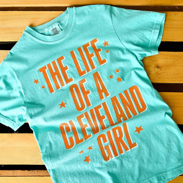 Turquoise t-shirt with 'The Life of a Cleveland Girl' text on a wooden surface