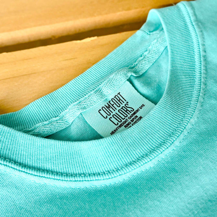 Close-up of a turquoise shirt with a Comfort Colors label on a wooden surface