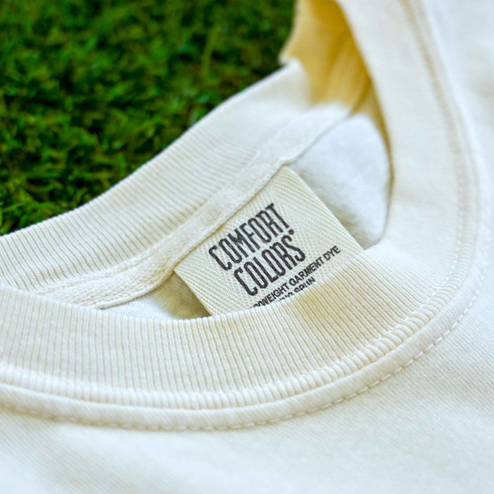 Close-up of a white garment with 'Comfort Colors' label against a blurred green background