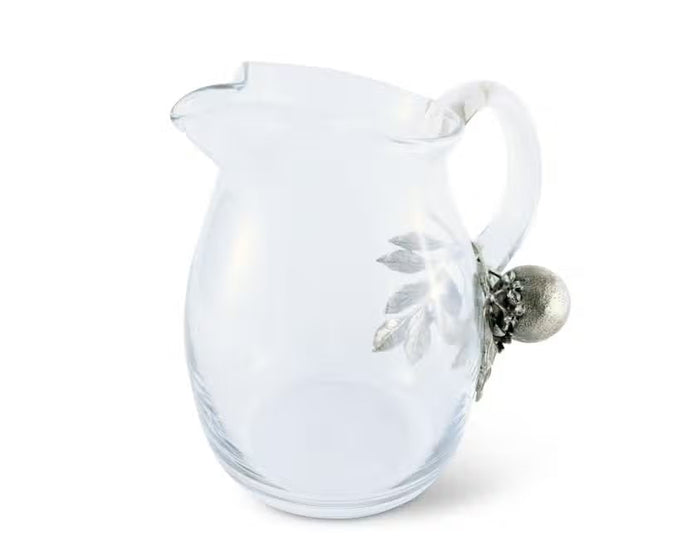 The VAGABOND HOUSE - ORANGE BLOOMS GLASS PITCHER features a clear glass design with a distinctive handle adorned in luxury-grade pewter, showcasing metallic textured oranges and leaves, creating an elegant contrast to the simple transparency of the pitcher.