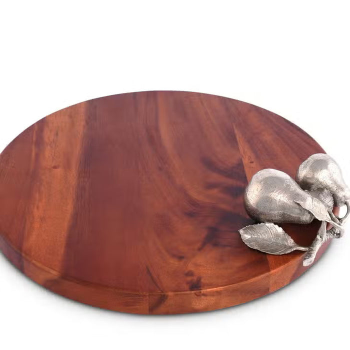 The VAGABOND HOUSE PEAR CHEESE TRAY is a round wooden cutting board with a smooth surface made from richly colored wood. It features two small decorative pears resembling pure-pewter designs on the right side, set against a plain white background, highlighting its elegance.