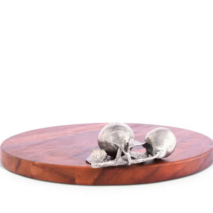 The VAGABOND HOUSE PEAR CHEESE TRAY is a round wooden cutting board with a smooth surface made from richly colored wood. It features two small decorative pears resembling pure-pewter designs on the right side, set against a plain white background, highlighting its elegance.