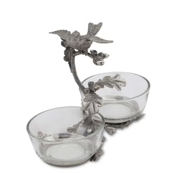 The VAGABOND HOUSE - SONG BIRD DOUBLE CONDIMENT BOWL features two glass bowls on an elegant metal stand adorned with ornate leaves and branches, topped by a pewter songbird.