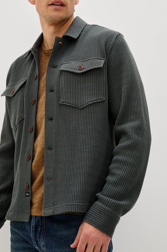 The Wells is a collared button front shirt jacket with contrast brown buttons and two chest pockets in Ink colorway. Front detail view featured on model.